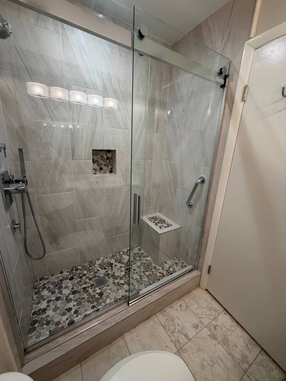 Glass walk-in shower with pebble floor, marble tile and corner seat