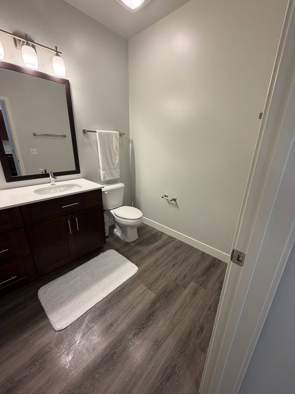 Bathroom with dark wood vanity, framed mirror and white bath mat