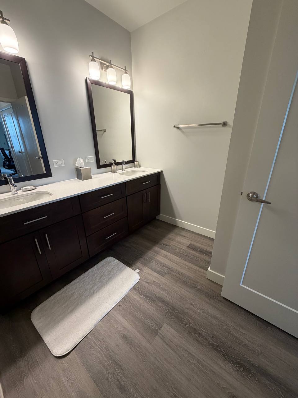 Double sink bathroom with dark cabinets and gray plank floor