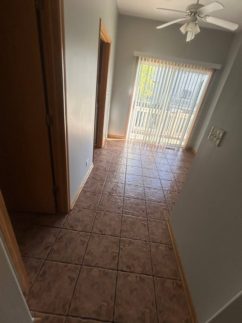 Empty room with brown tile floor, ceiling fan and sliding door