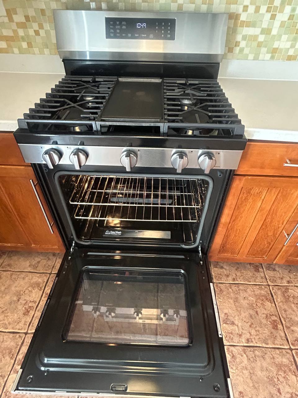 Stainless gas range with open oven, clean racks and tile floor