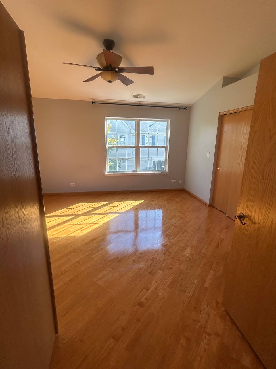 Sunlit empty room with light hardwood floor and ceiling fan