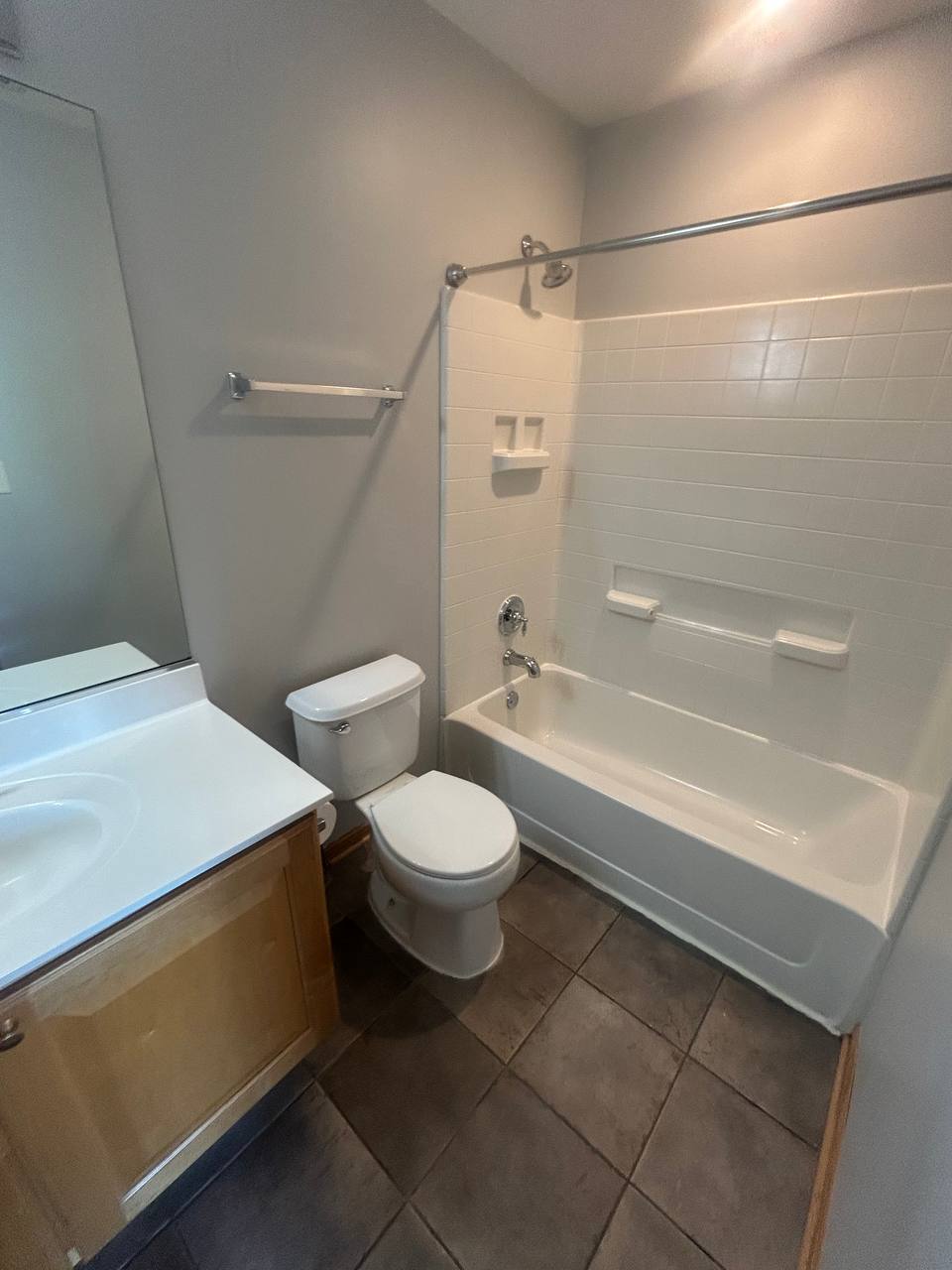 Gray bathroom with white tub shower, toilet and oak vanity