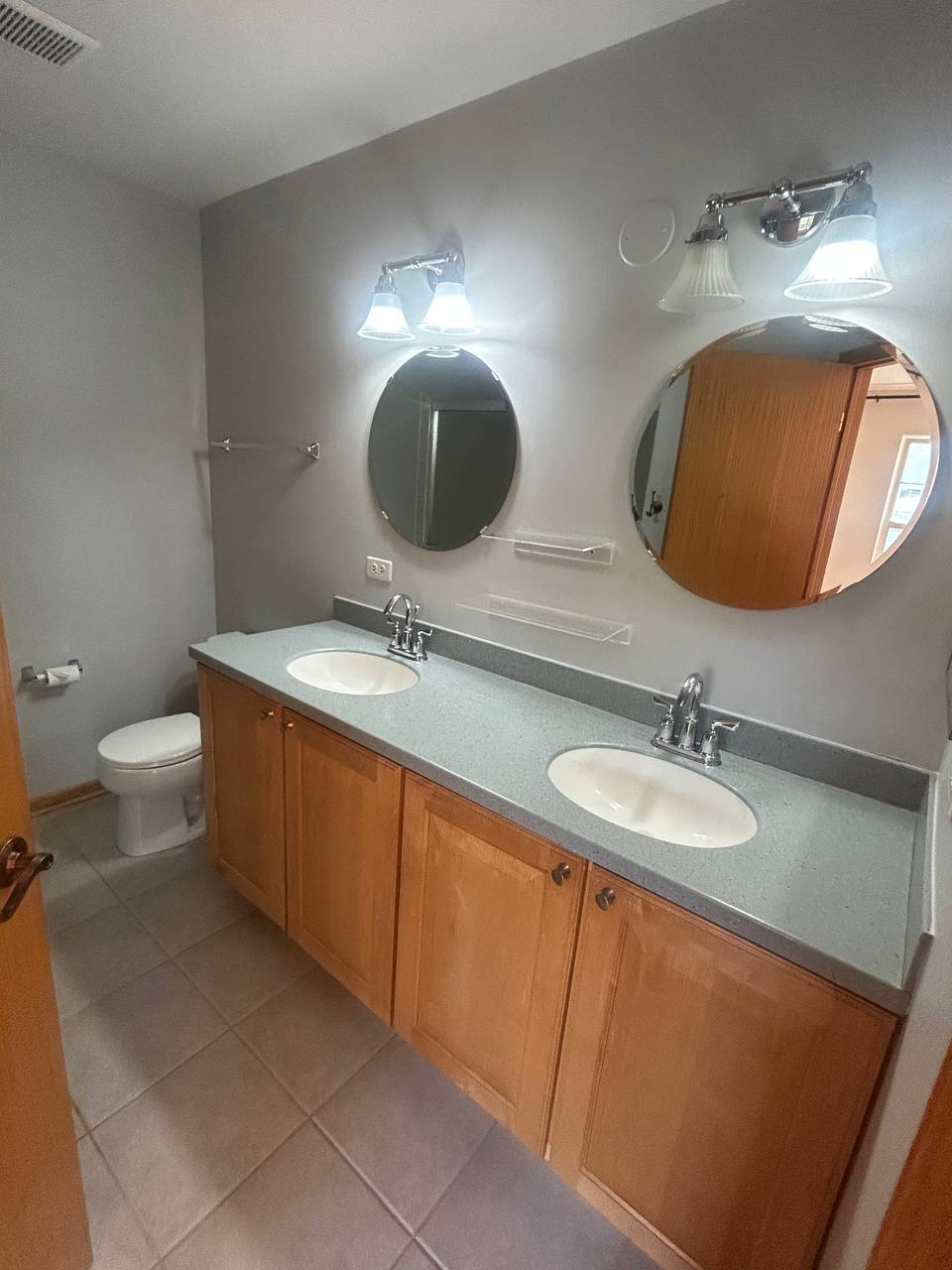 Bathroom with light wood double vanity, gray counter and round mirrors