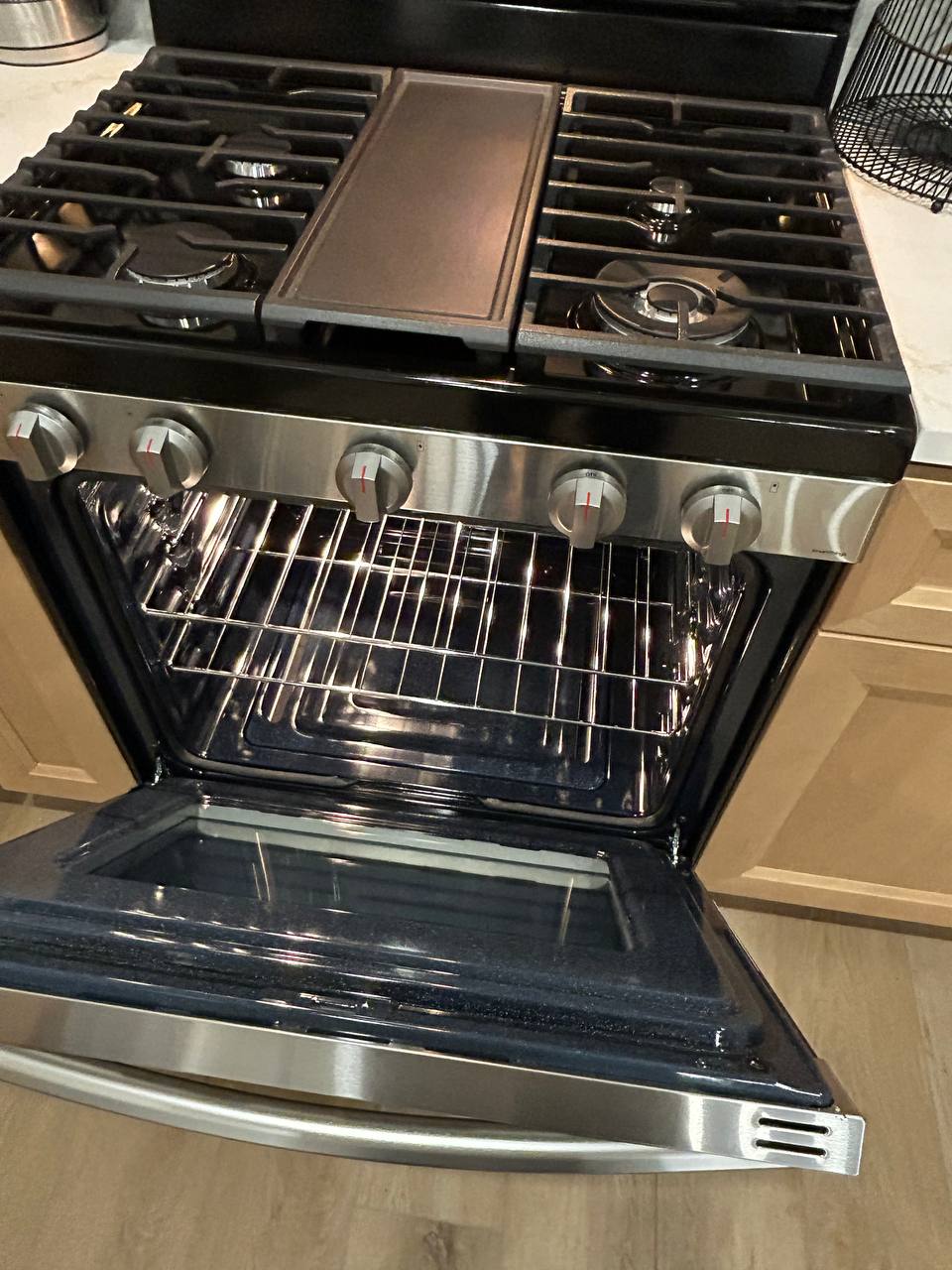 Stainless gas range with oven door open showing clean racks