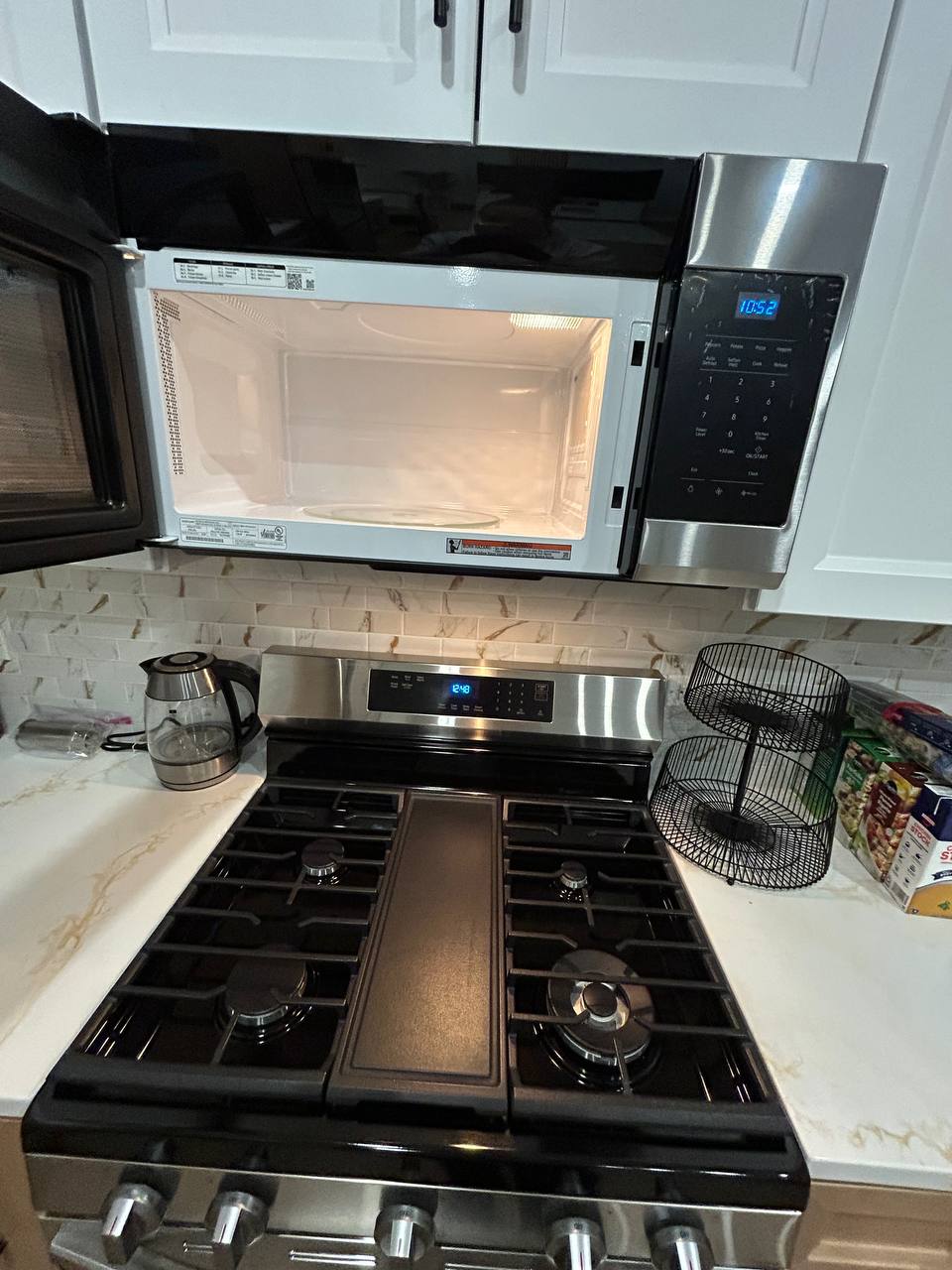 Open stainless microwave above a gas range with marble backsplash and kettle