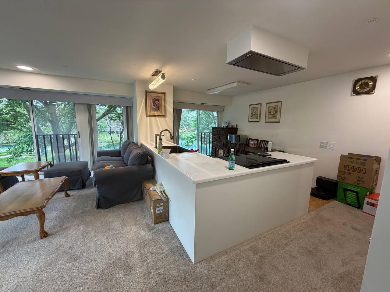 Open living room with gray sofa, white kitchen peninsula and patio doors