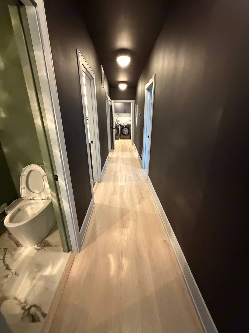 Long hallway with dark walls, light wood floor and laundry room