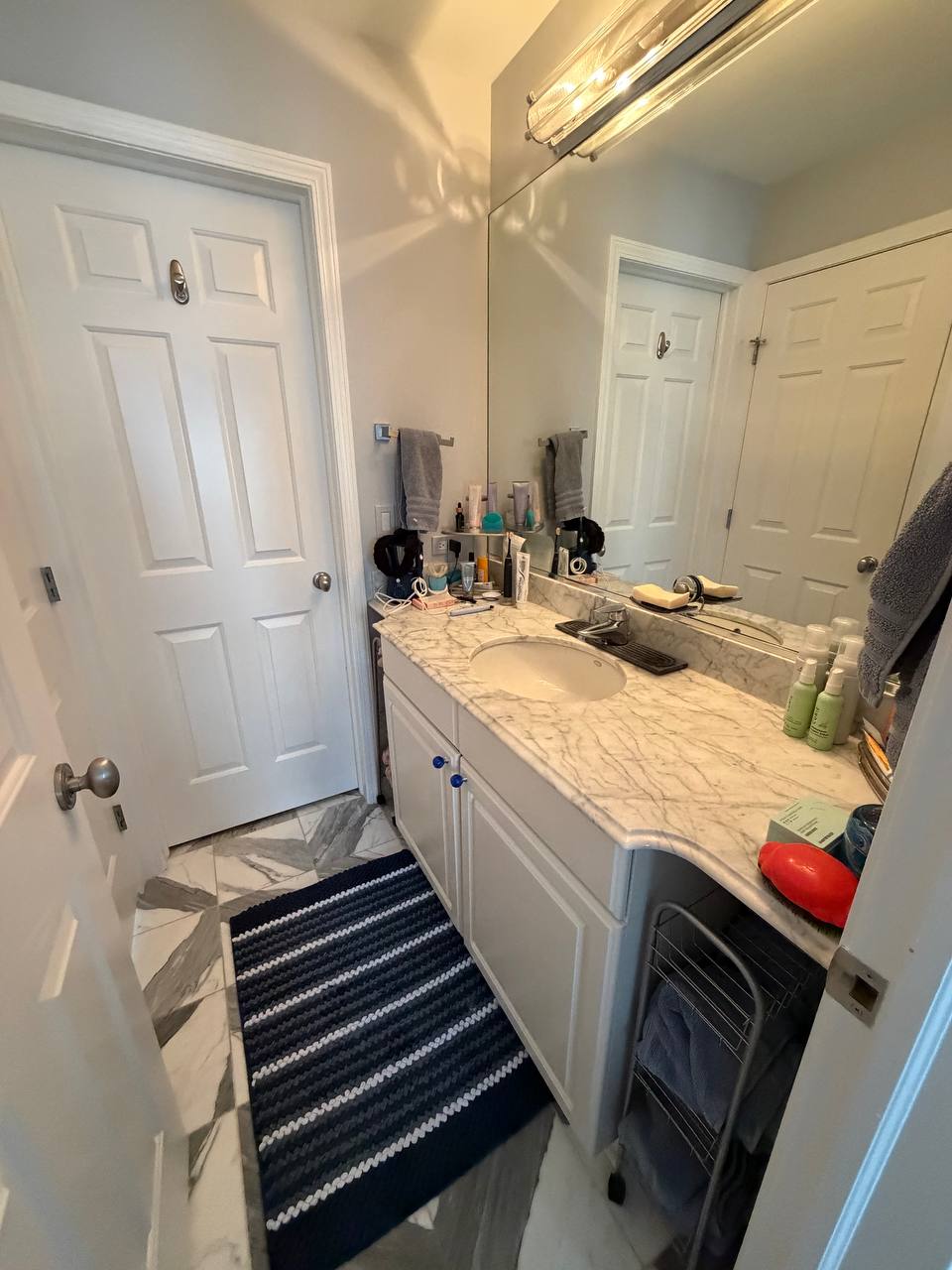 Narrow bathroom with marble counter, striped rug and white doors