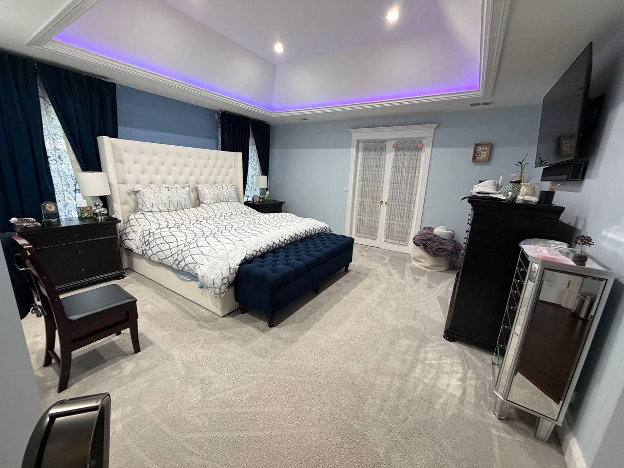 Large bedroom with white tufted bed, navy bench and lit tray ceiling