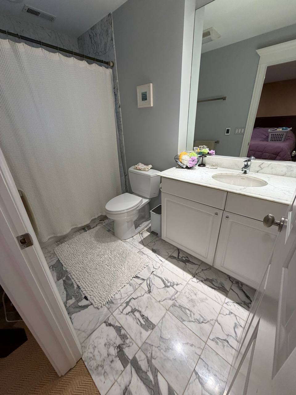 Bathroom with marble floor, white vanity and waffle shower curtain