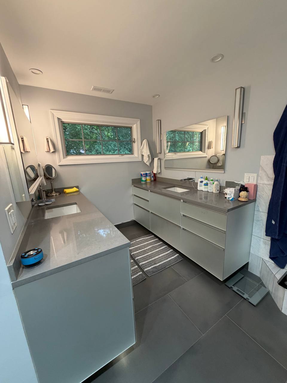 Modern bathroom with two gray vanities, window and dark tile floor
