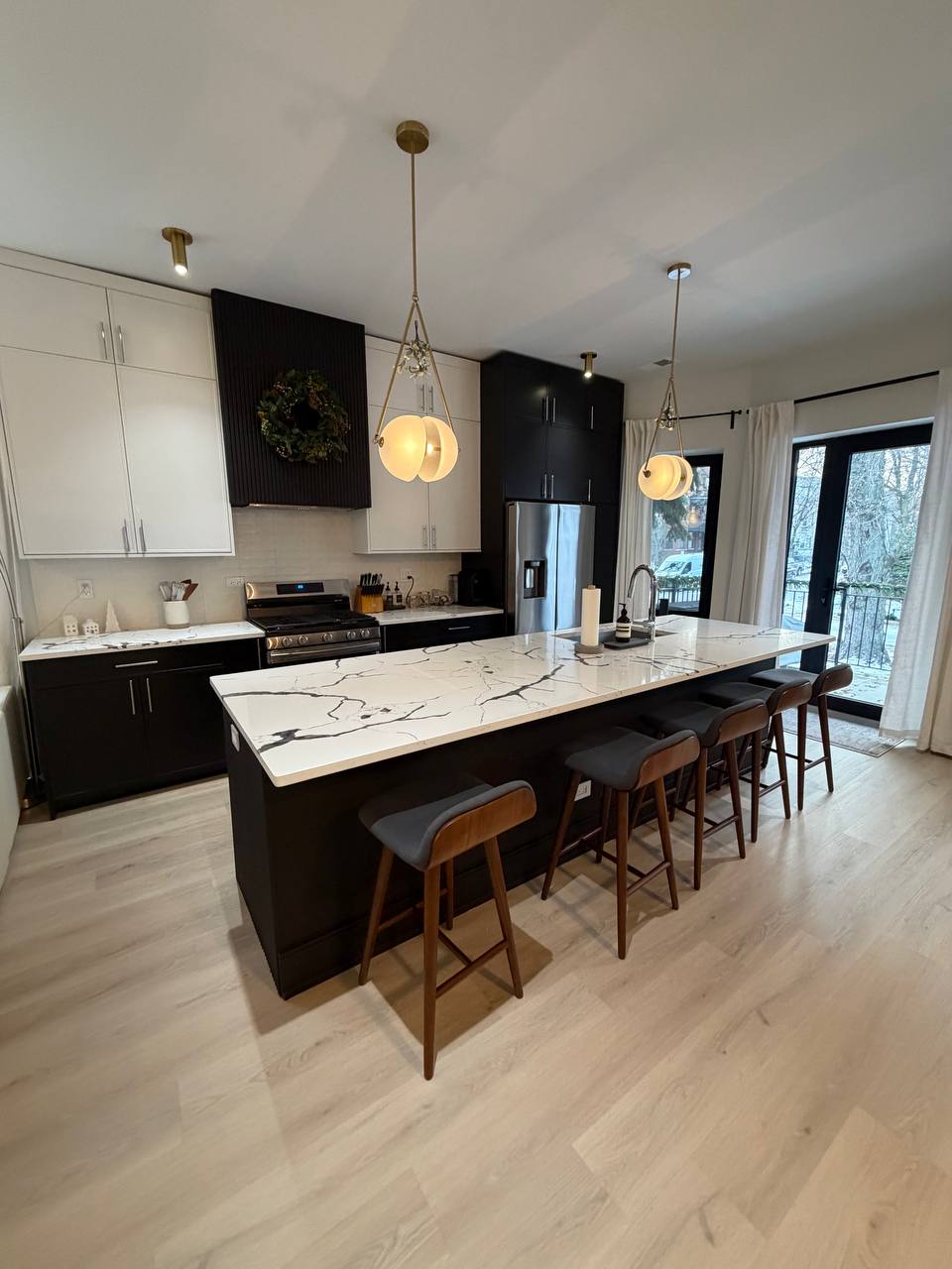 Kitchen with marble island, five wood stools and brass pendant lights