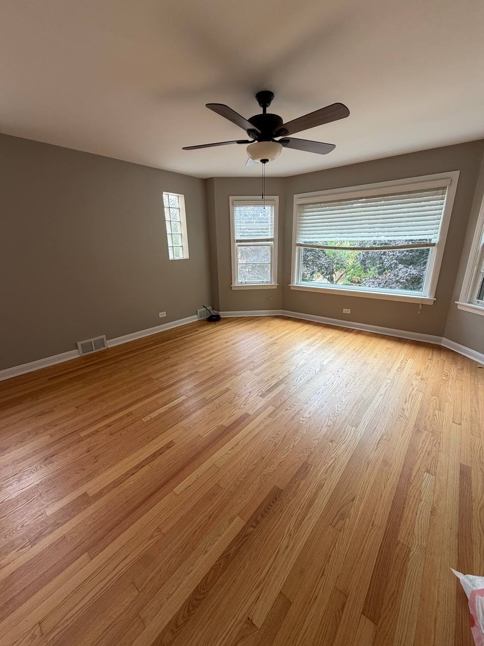 Empty room with light hardwood floor, ceiling fan and bay windows