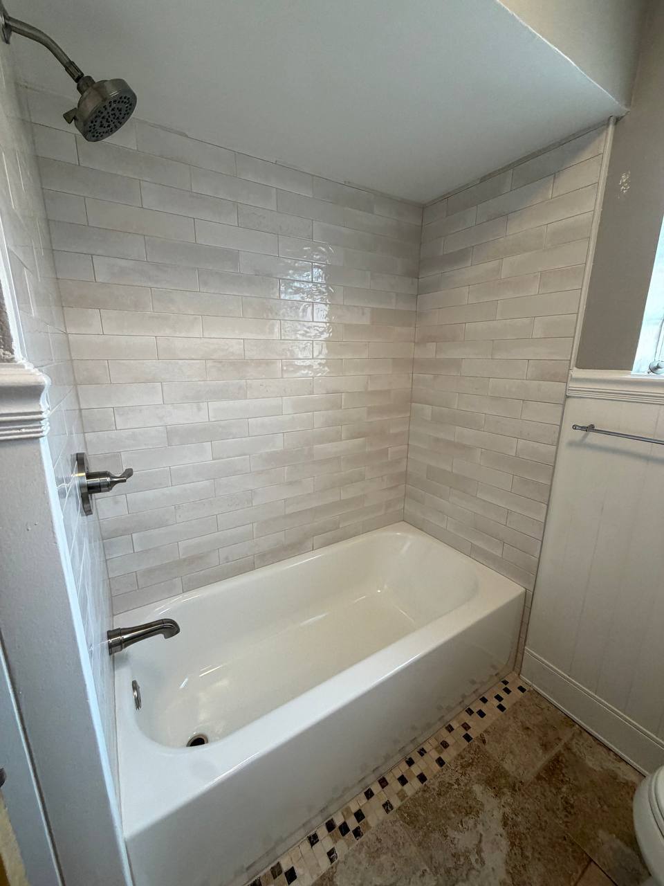 White bathtub with light subway tile surround and brushed fixtures
