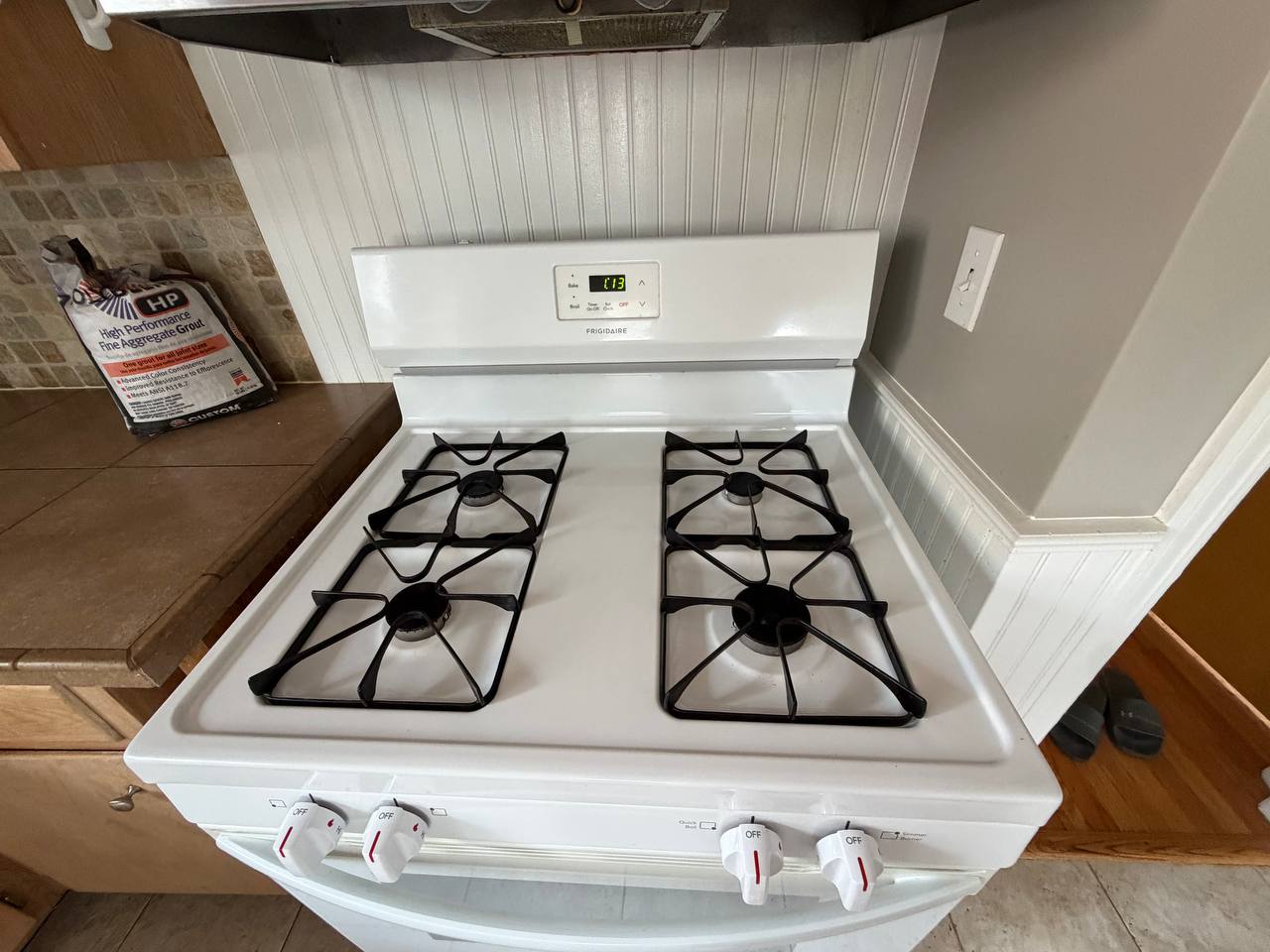 White gas range with four black burner grates against beadboard wall