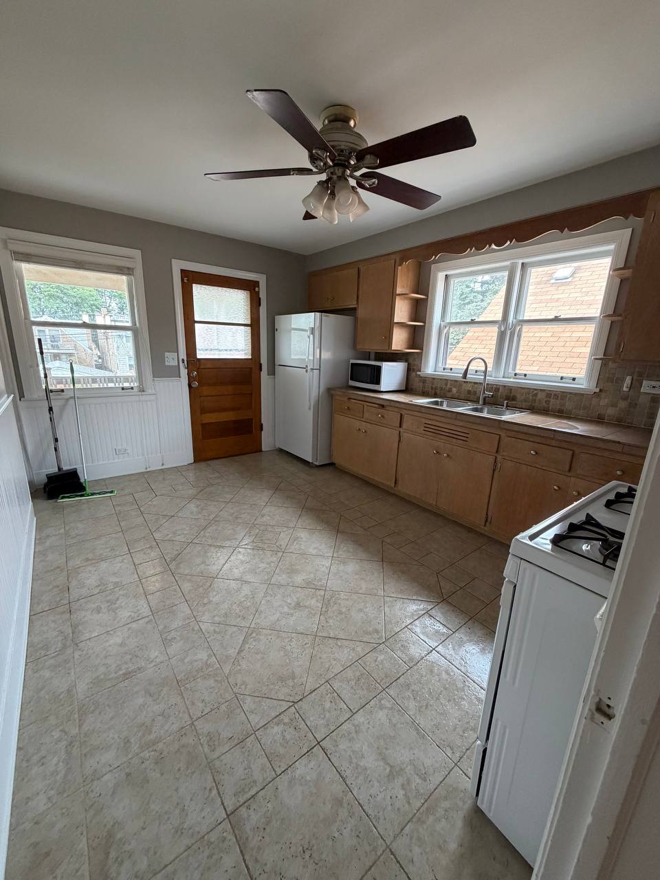 Empty kitchen with light wood cabinets, white fridge and tile floor
