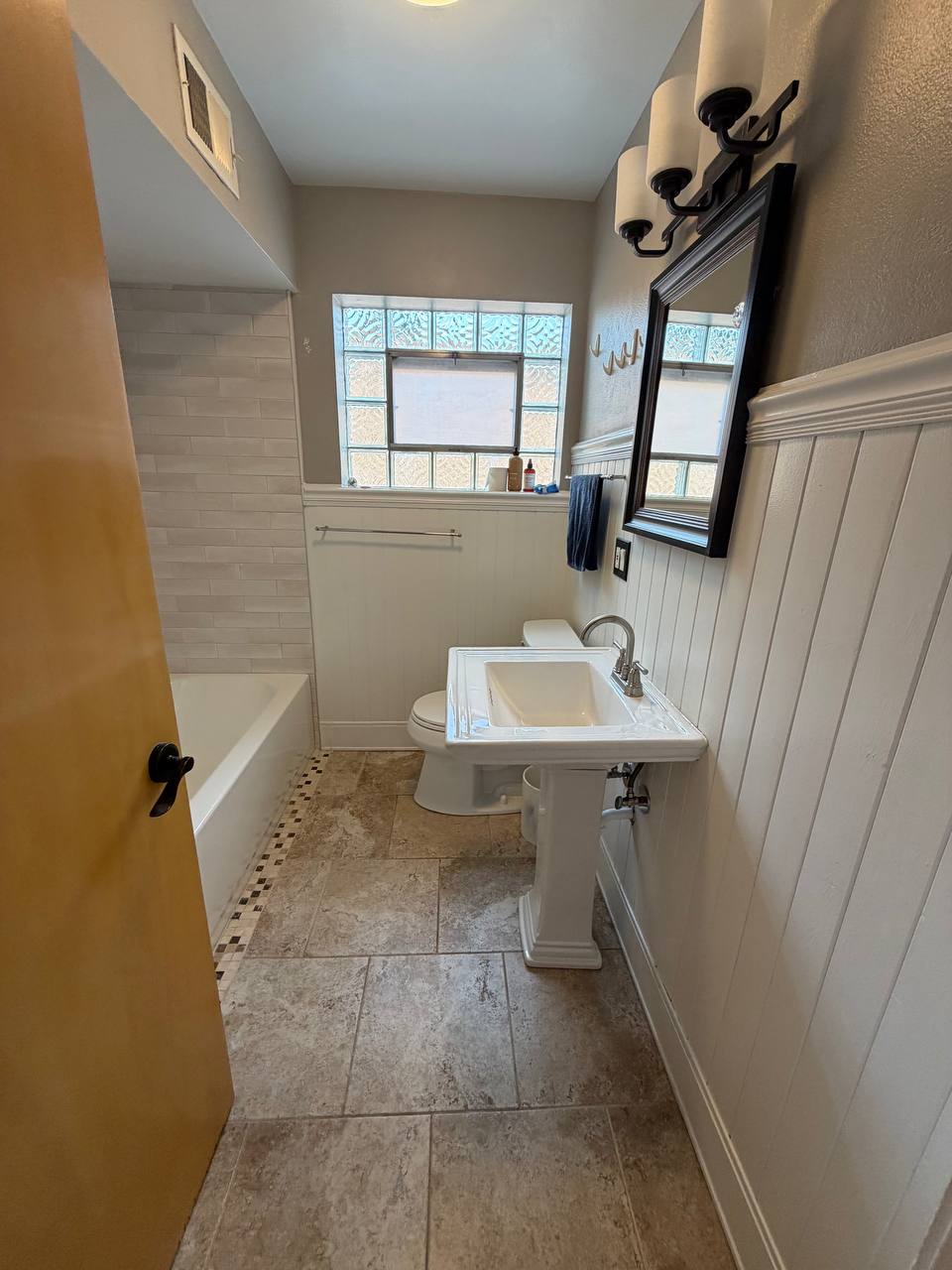 Bathroom with pedestal sink, glass block window and white paneled walls