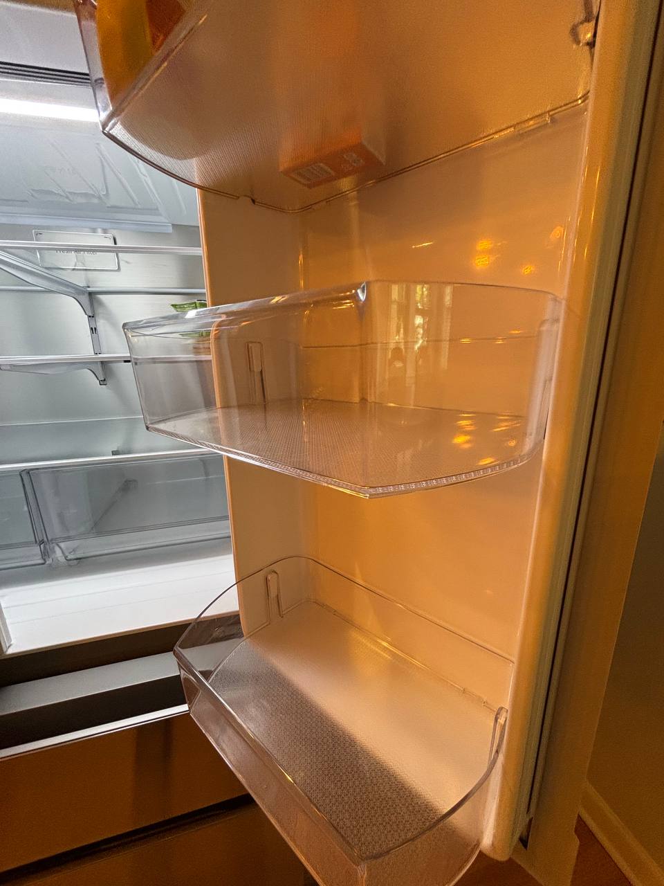 Empty refrigerator door with clear bins and lit shelves
