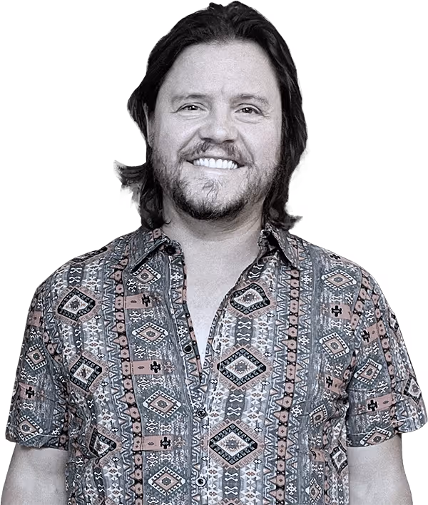 Black & white photograph of Chris Moseman smiling and looking into the camera. Wearing a complex pattern collared button-down shirt with short sleeves.