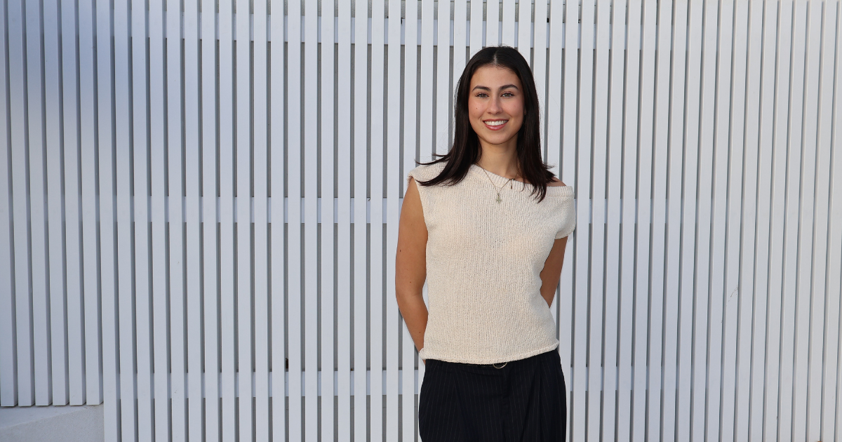 A professional photo of Amina Powditch, founder of In Sync Creative, smiling confidently against a clean vertical panel backdrop. This image conveys approachability, creative confidence, and modern branding—perfectly aligned with In Sync Creative’s mission to deliver design, content, and digital services with clarity and impact.