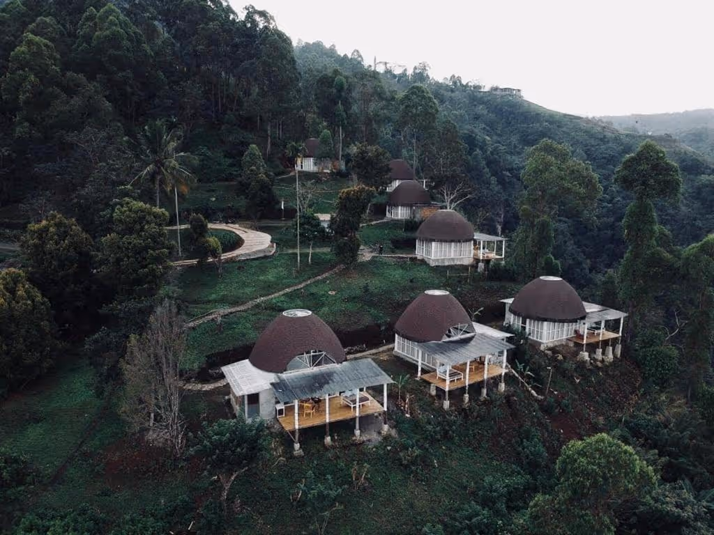 Cluster of dome-shaped Manulalu Jungle bungalows with porches on a green hillside surrounded by dense trees and forest.