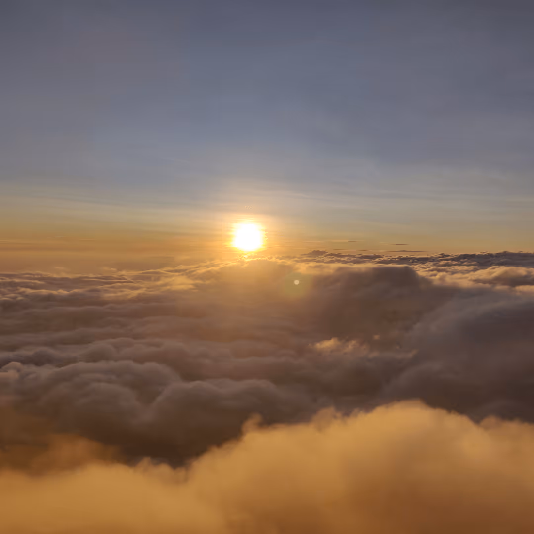 Sunset or sunrise over a sea of fluffy clouds with a clear sky above.