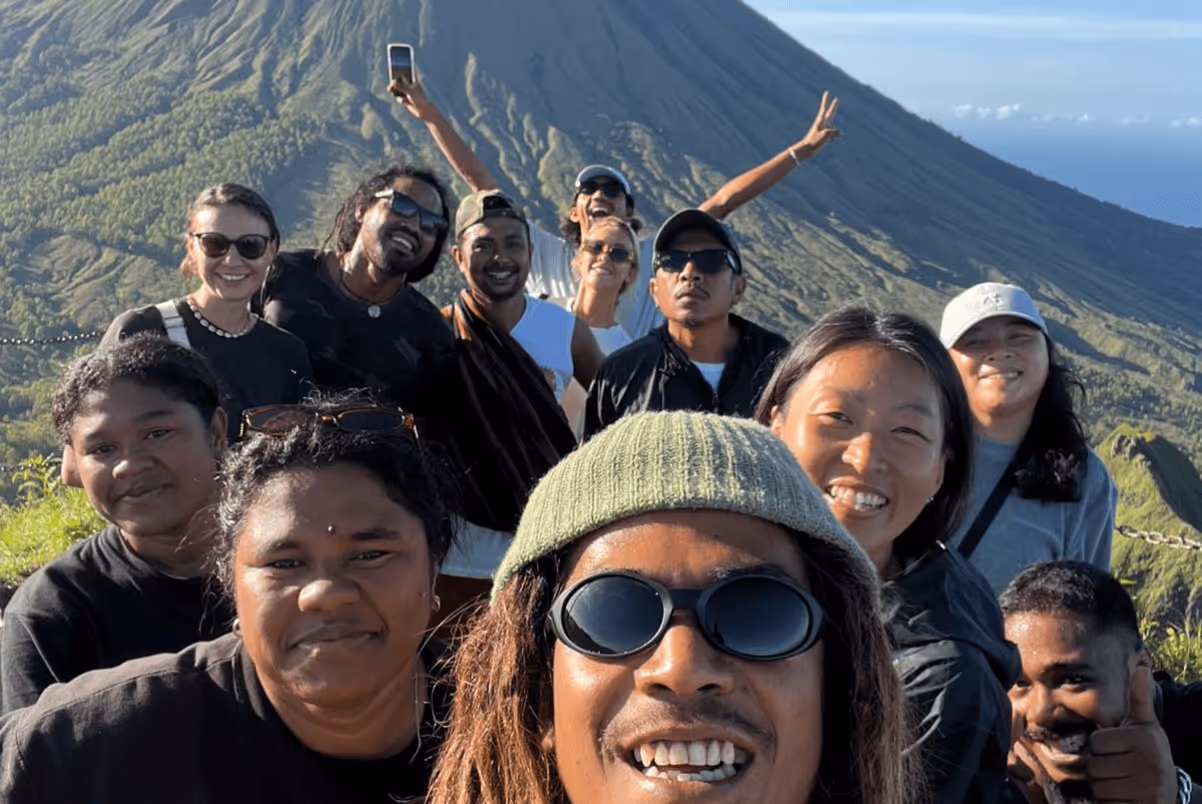 Group of smiling people outdoors posing for a selfie with a mountain in the background.