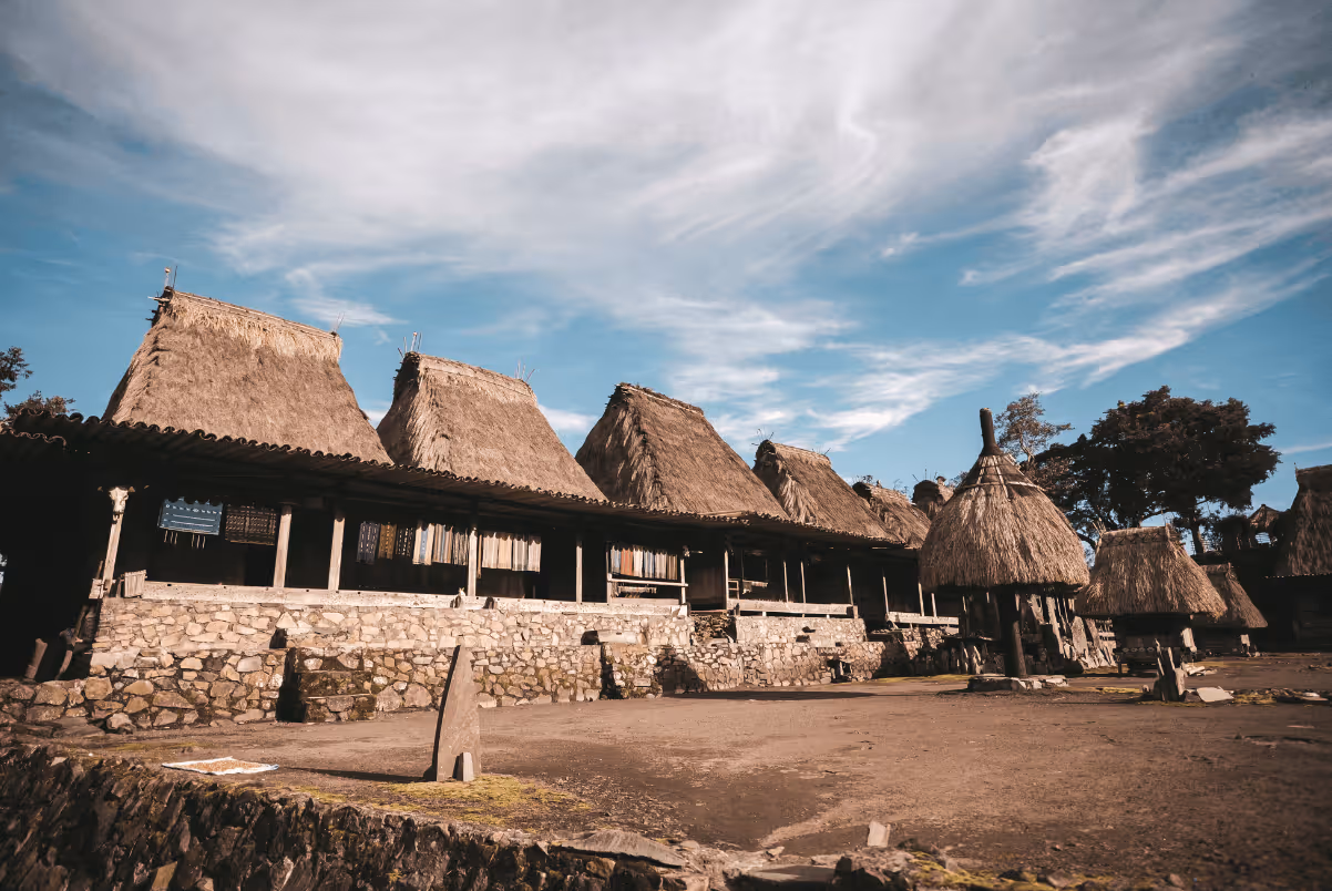 Traditional thatched-roof houses with stone foundations under a partly cloudy sky.