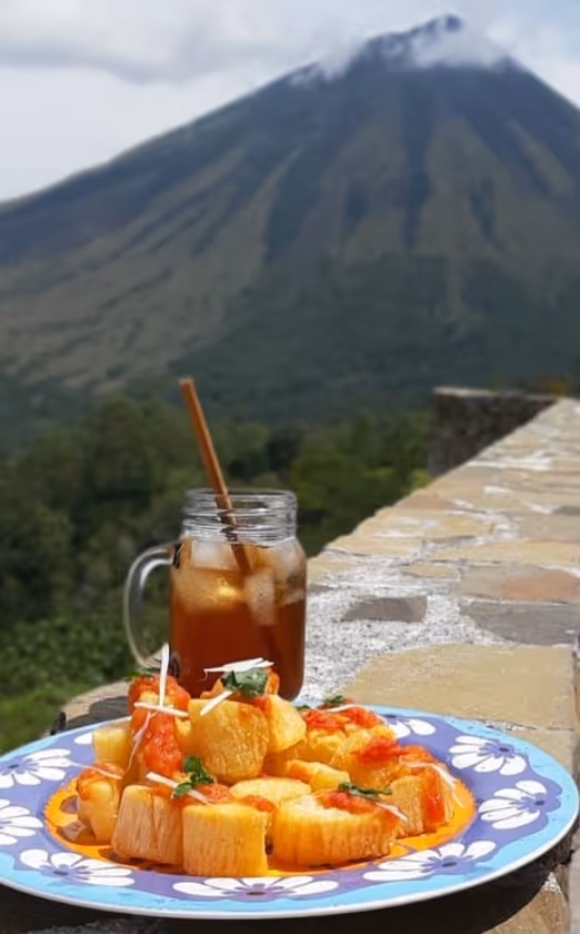 Plate of yellow fried food garnished with herbs on a floral plate with a glass of iced tea and a mountain in the background.