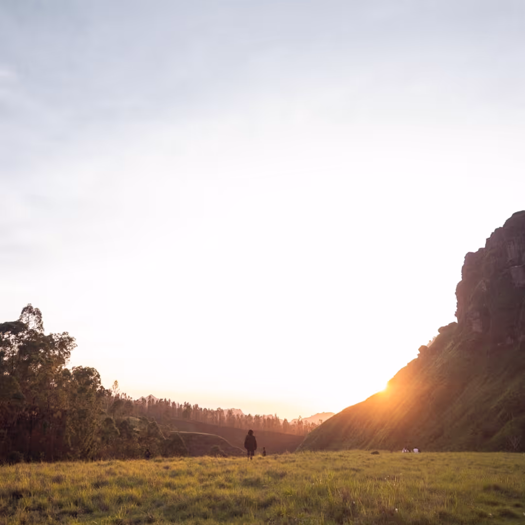 Sunset over grassy field with people walking and hills in the background.