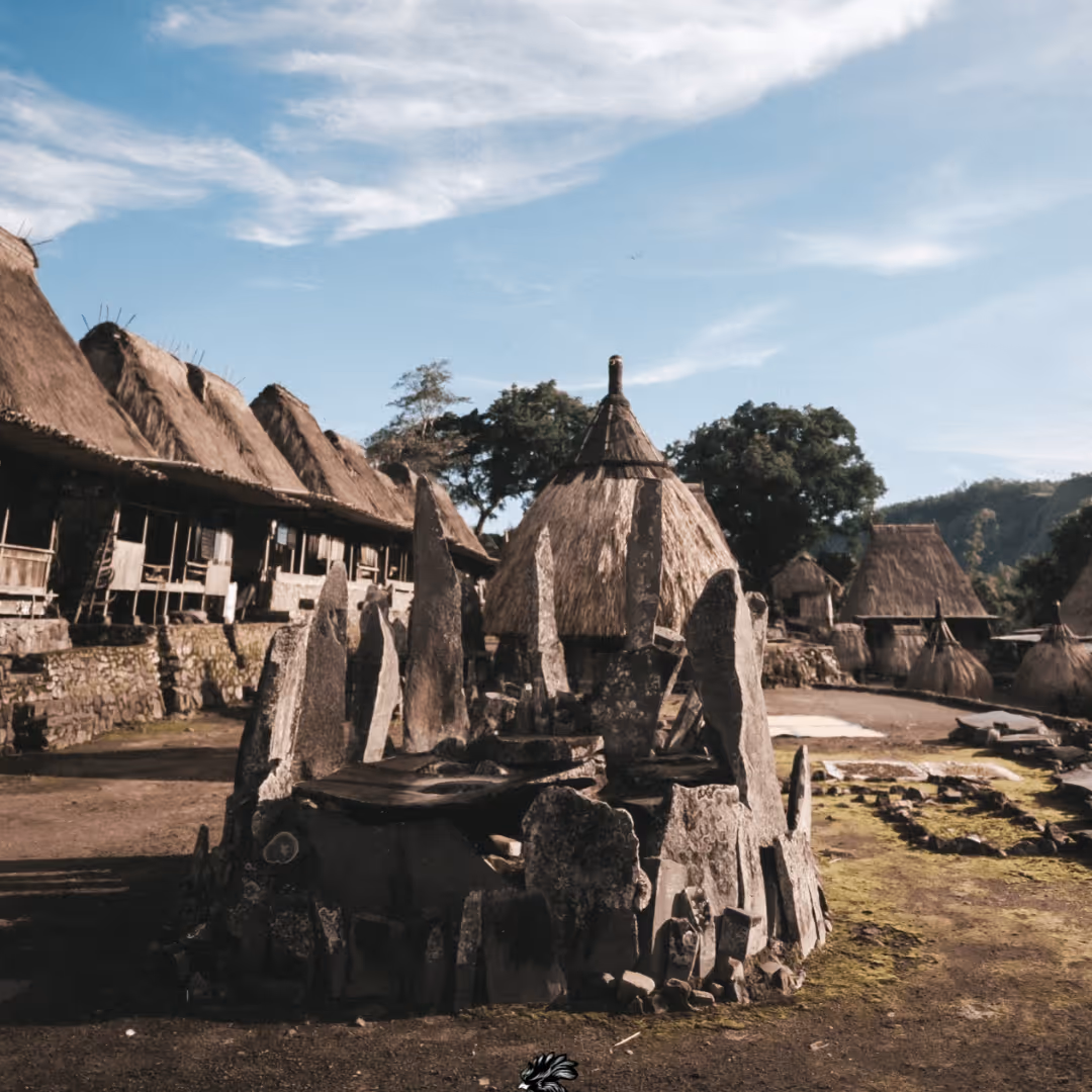 Traditional village with stone monument in the center and thatched-roof houses under a blue sky.