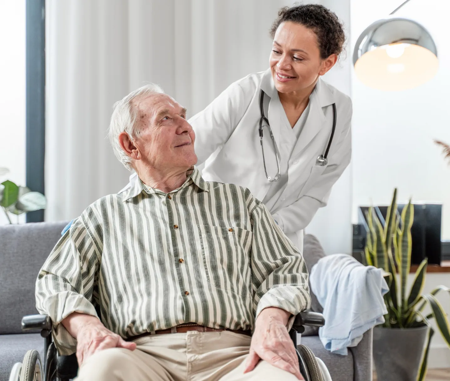 A woman in a white coat is talking to a man in a wheelchair.
