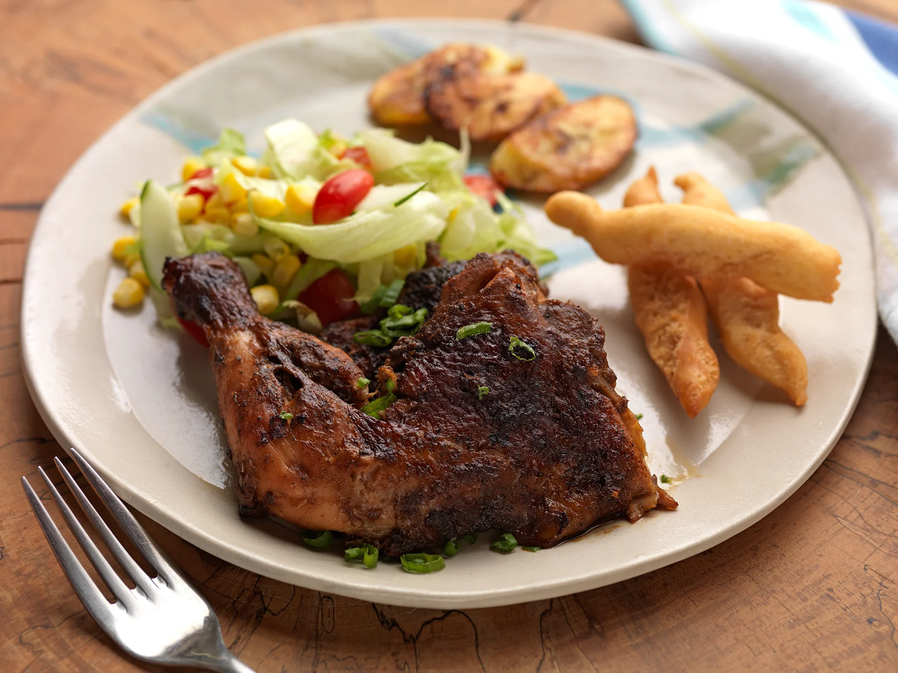 Plate of jerk chicken and festival garnished with herbs and a salad