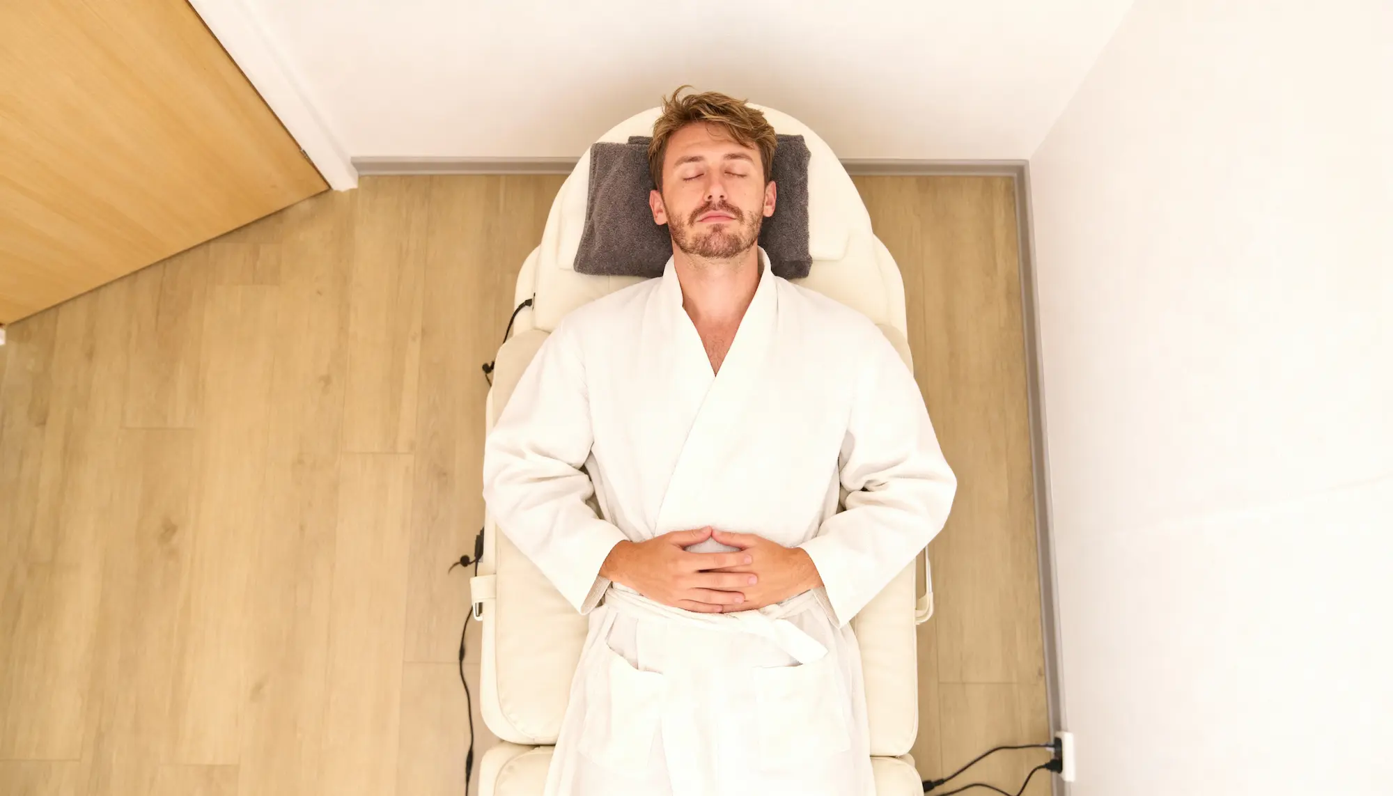 Homme allongé sur une table de massage, les yeux fermés, portant un peignoir blanc.