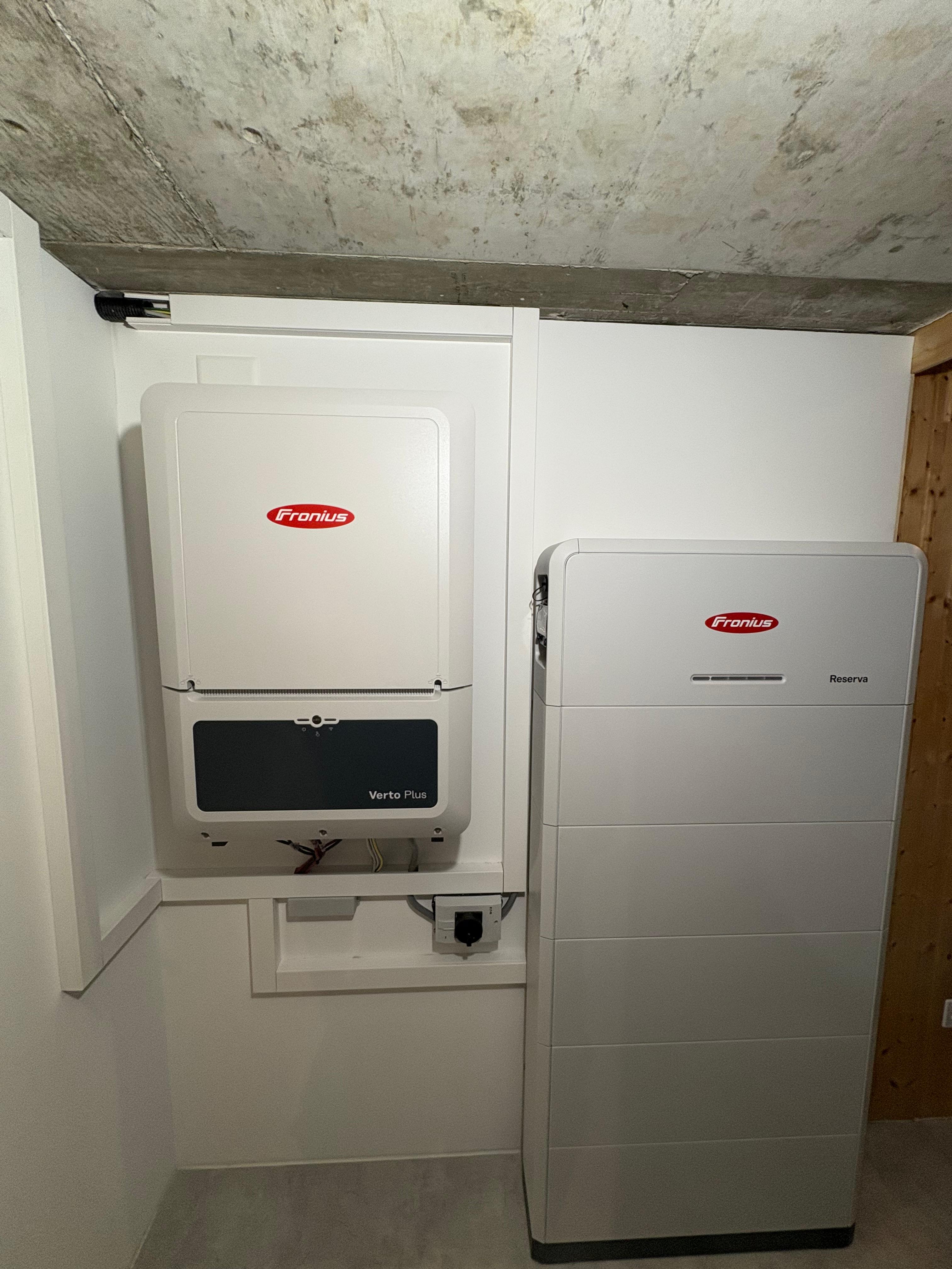 Weiss-graue Fronius Verto Plus Wechselrichter und Fronius Reserva Batteriespeicher in einem Raum mit Beton-Decke.