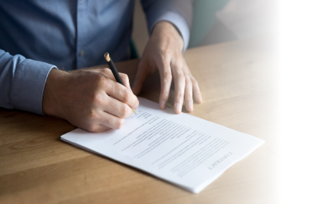 A close-up of a person's hands signing a document with a pen on a wooden desk.