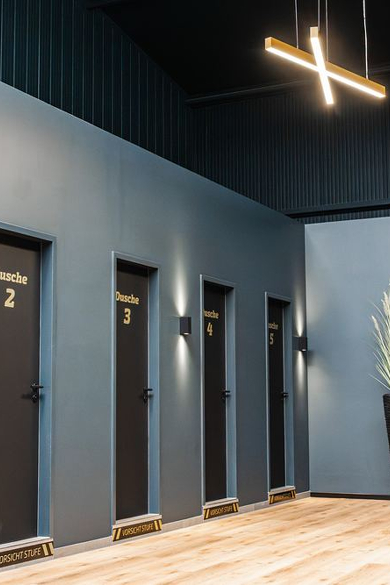 Row of four shower doors numbered 2 to 5 on a gray wall with wooden floor and modern lighting.