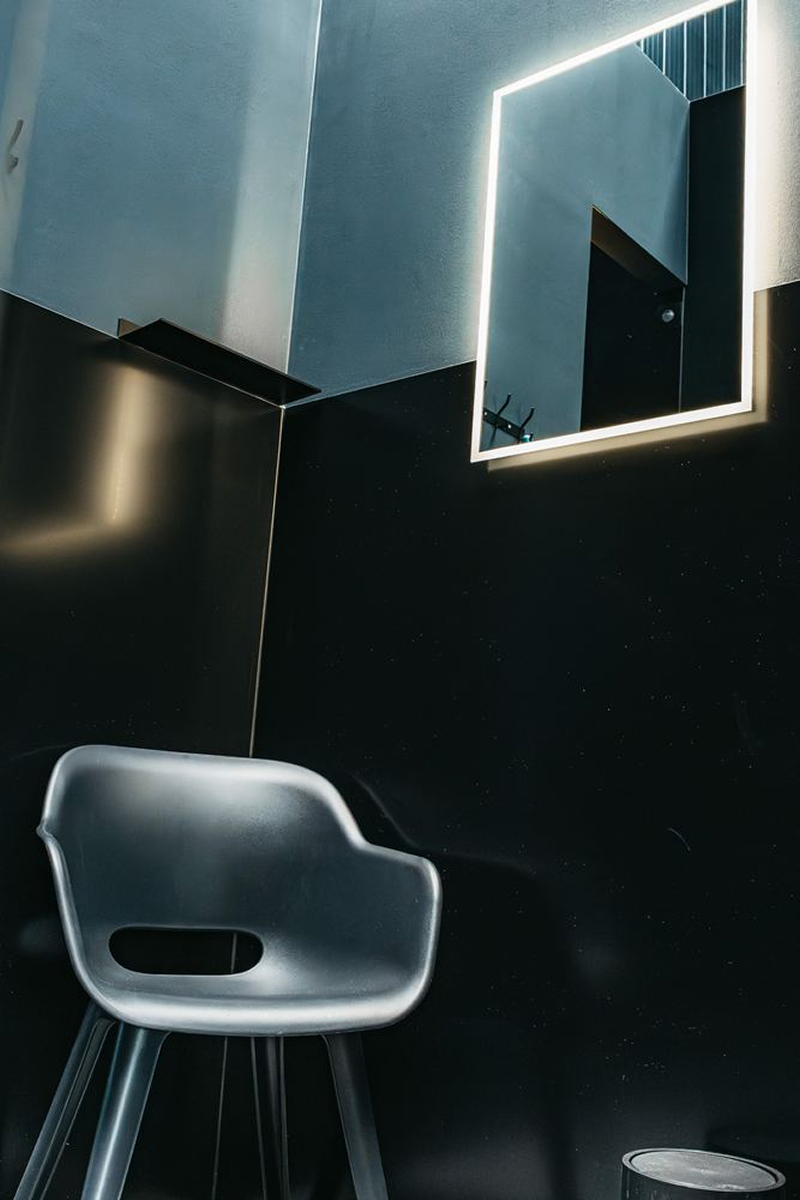 Modern black corner room with a black chair and a square mirror with bright LED border.