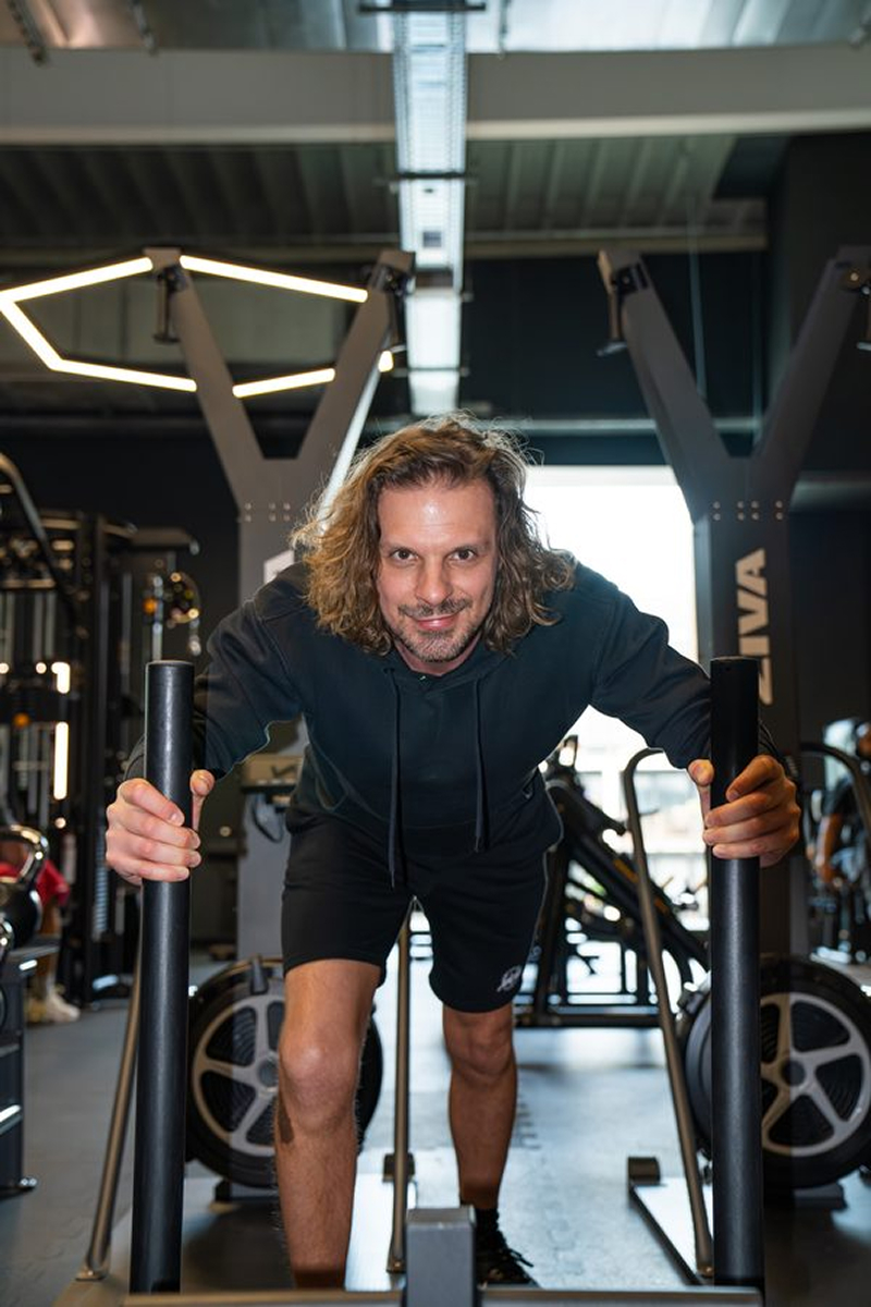 Man in black hoodie and shorts pushing sled workout equipment in gym.