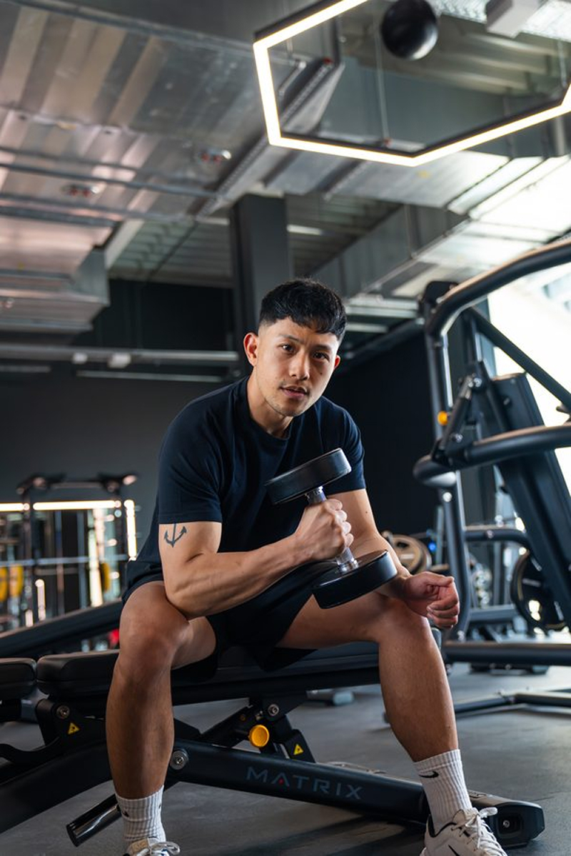 Man sitting on gym bench doing bicep curl with dumbbell in fitness center.