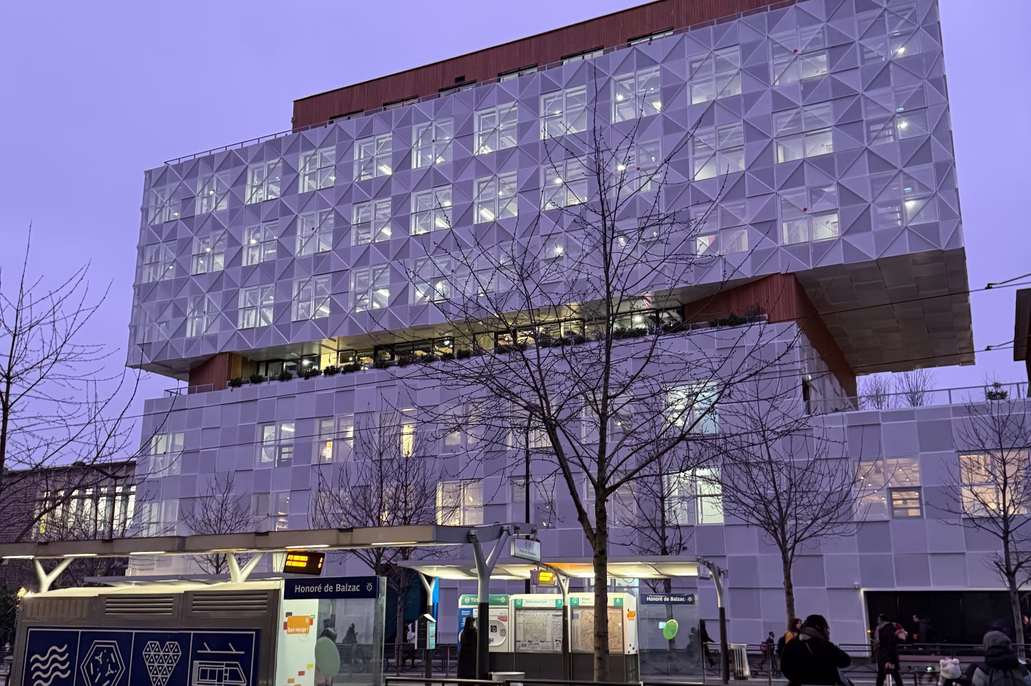 Ecole 42 - Bâtiment moderne avec façade en motifs géométriques éclairée au crépuscule à la station de métro Honoré de Balzac.