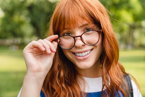 Smiling redhead with glasses adjusting eyewear in sunny outdoor setting