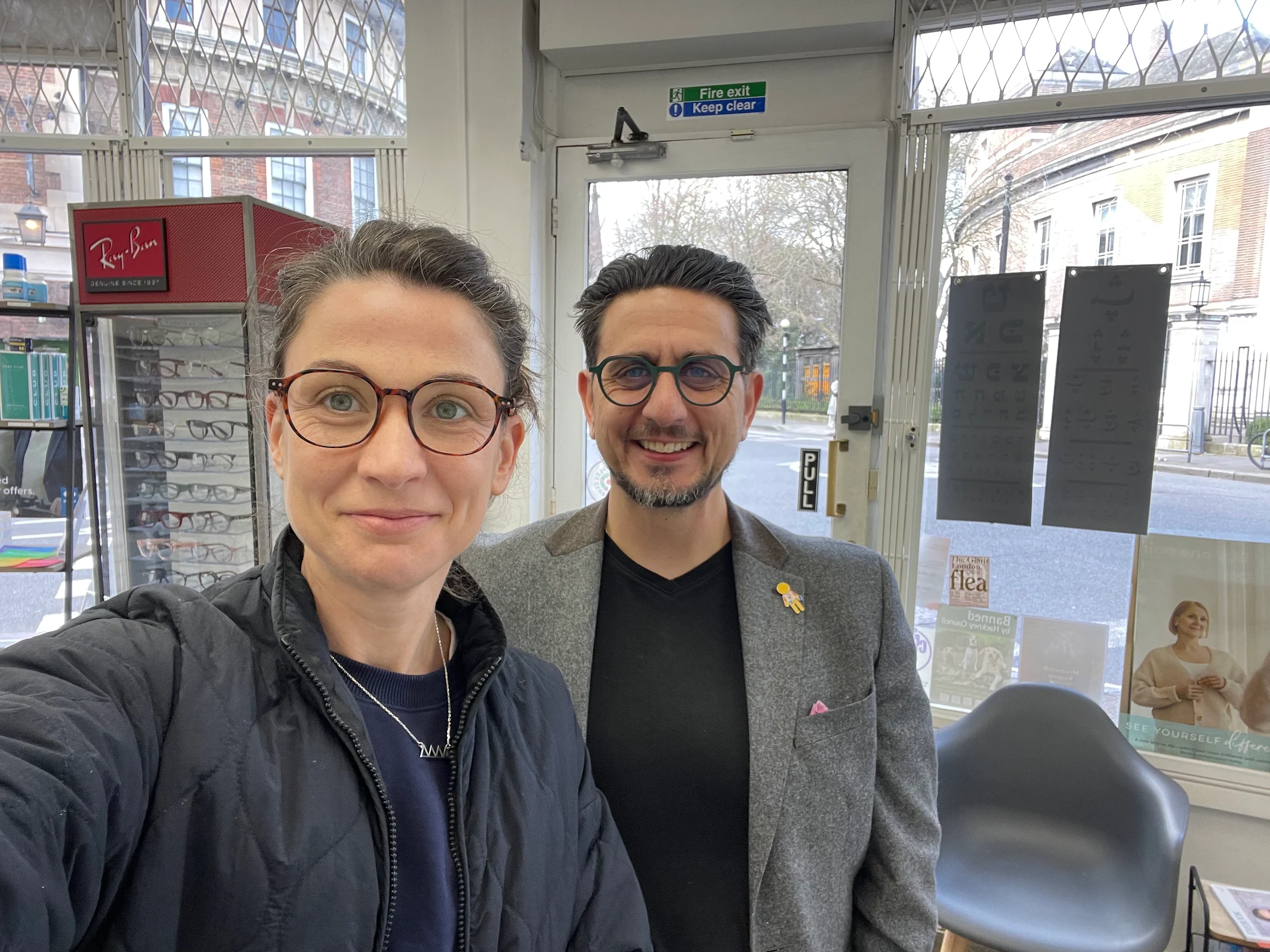 Two people smiling in an eyeglass store with Ray-Ban display