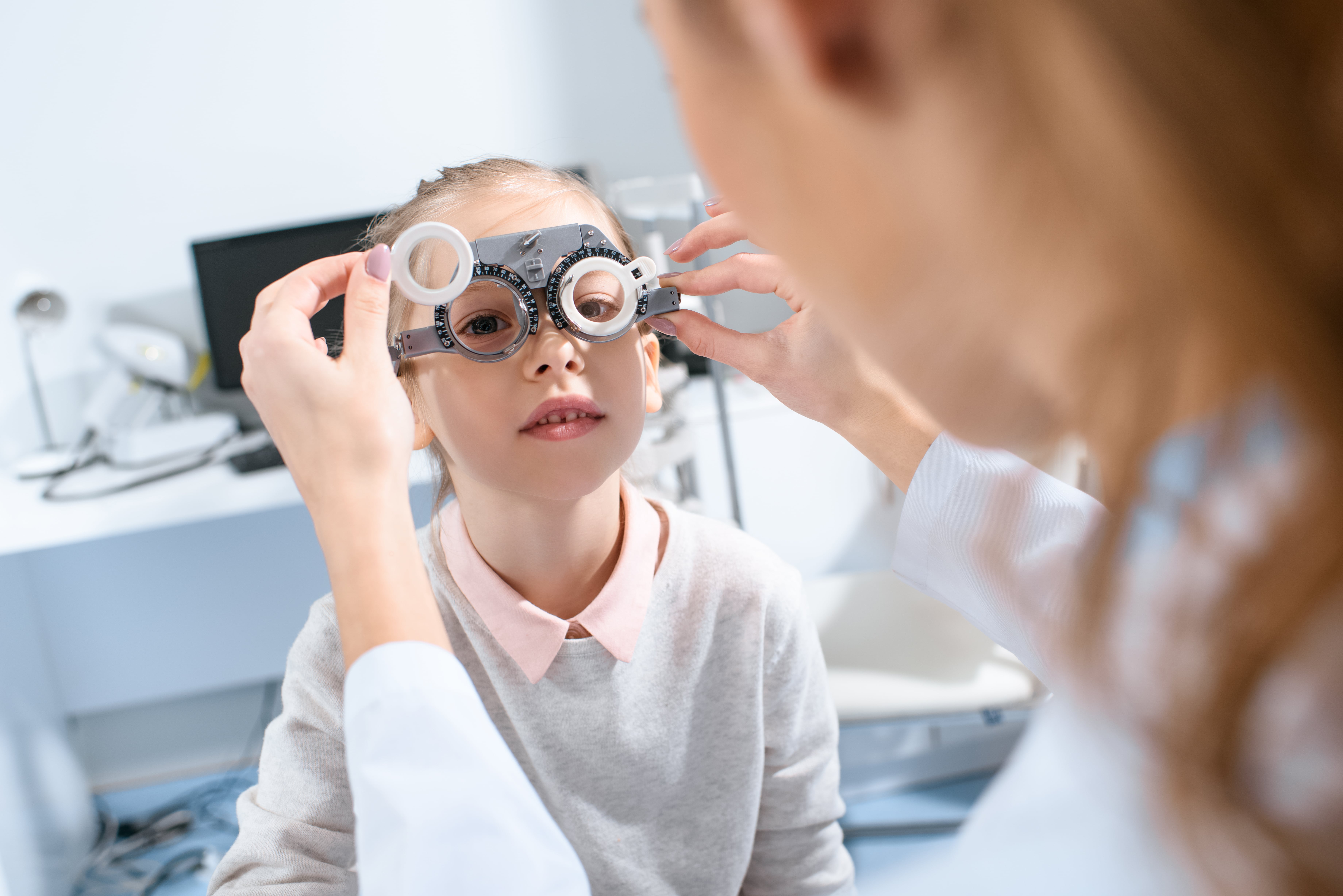 Child getting eye exam with optometry trial frame in medical office