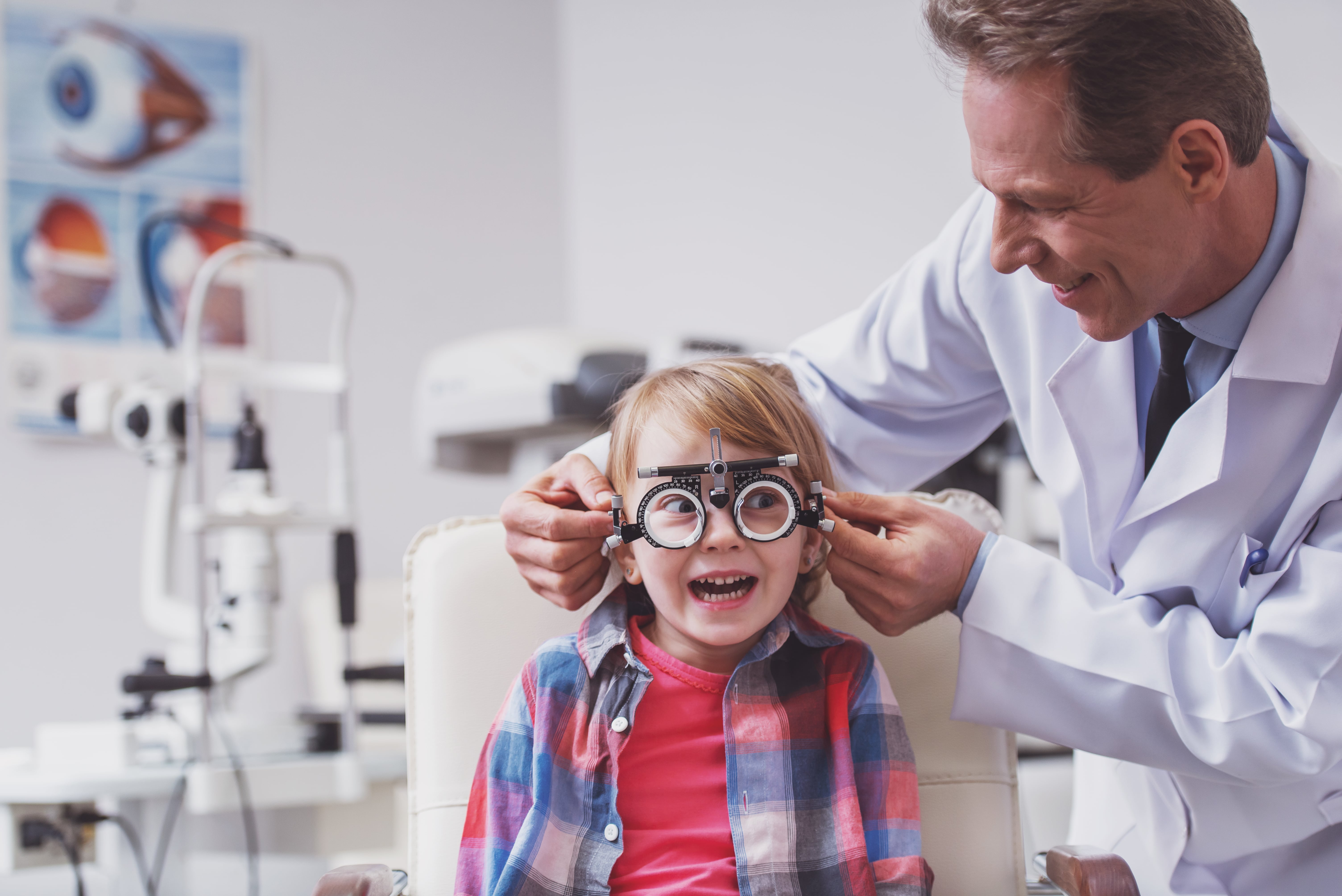 Smiling child getting eye exam with optometrist adjusting trial lens frame