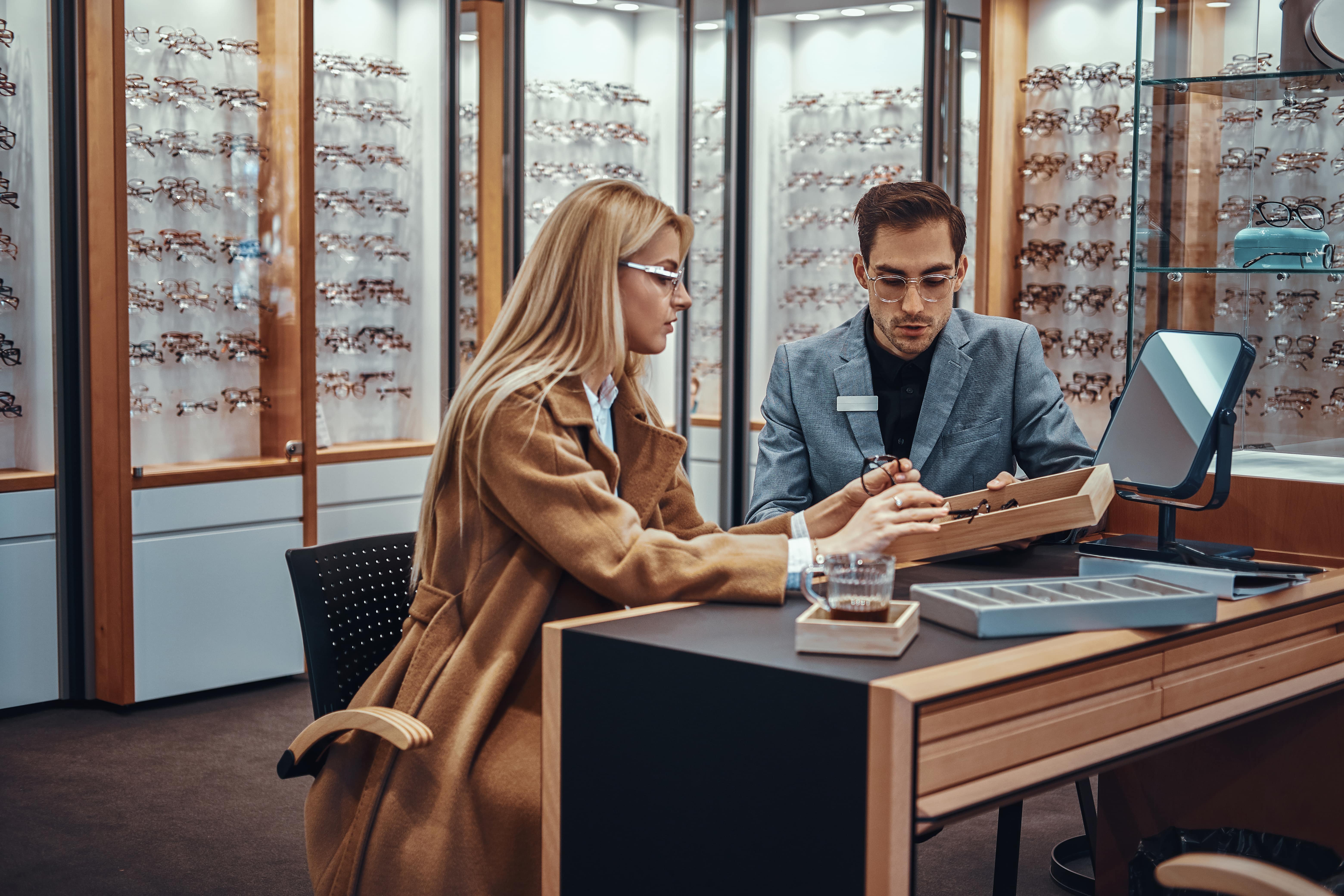 Optician helping customer choose glasses in modern eyewear store