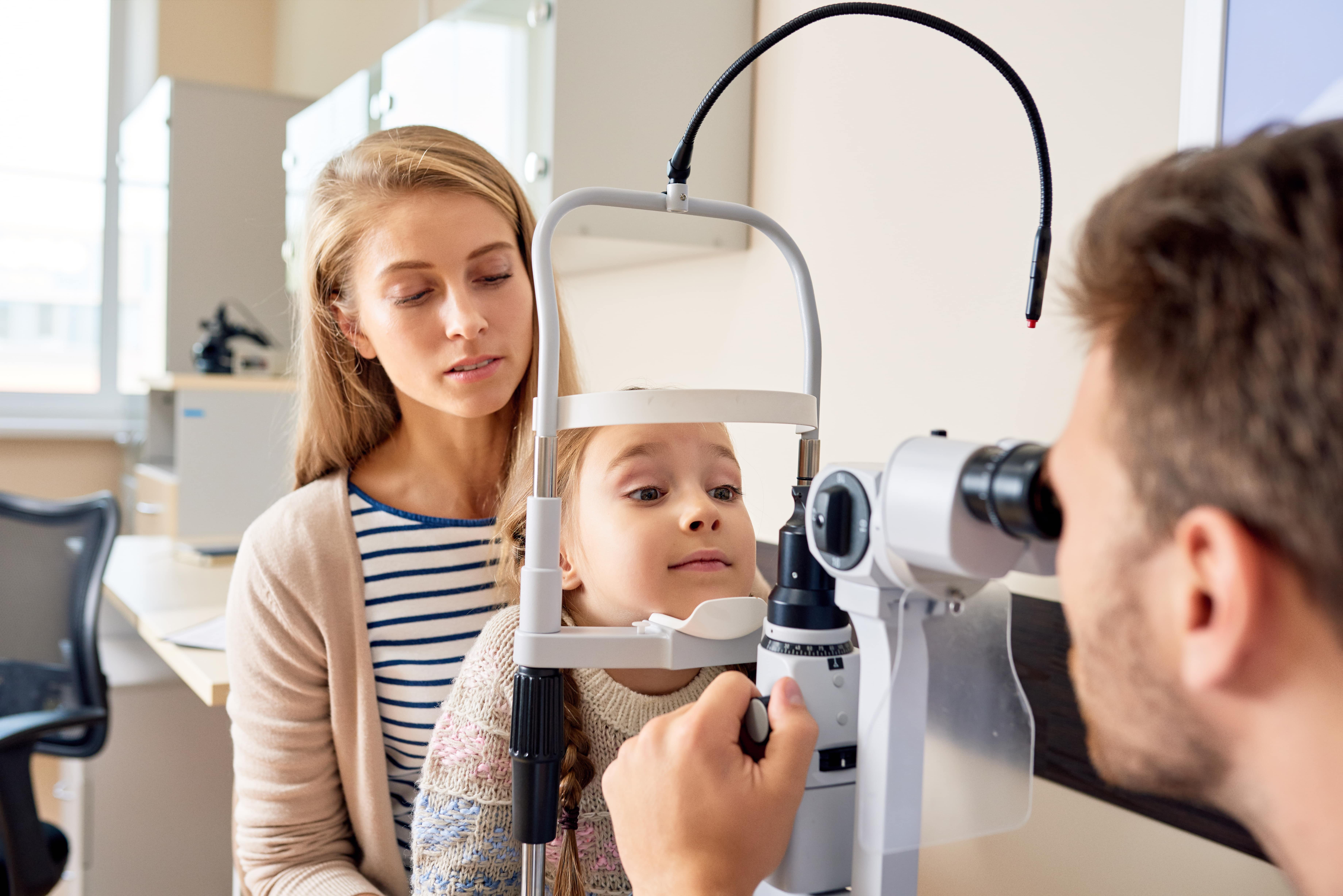 Child getting eye exam with mother at optometrist's office