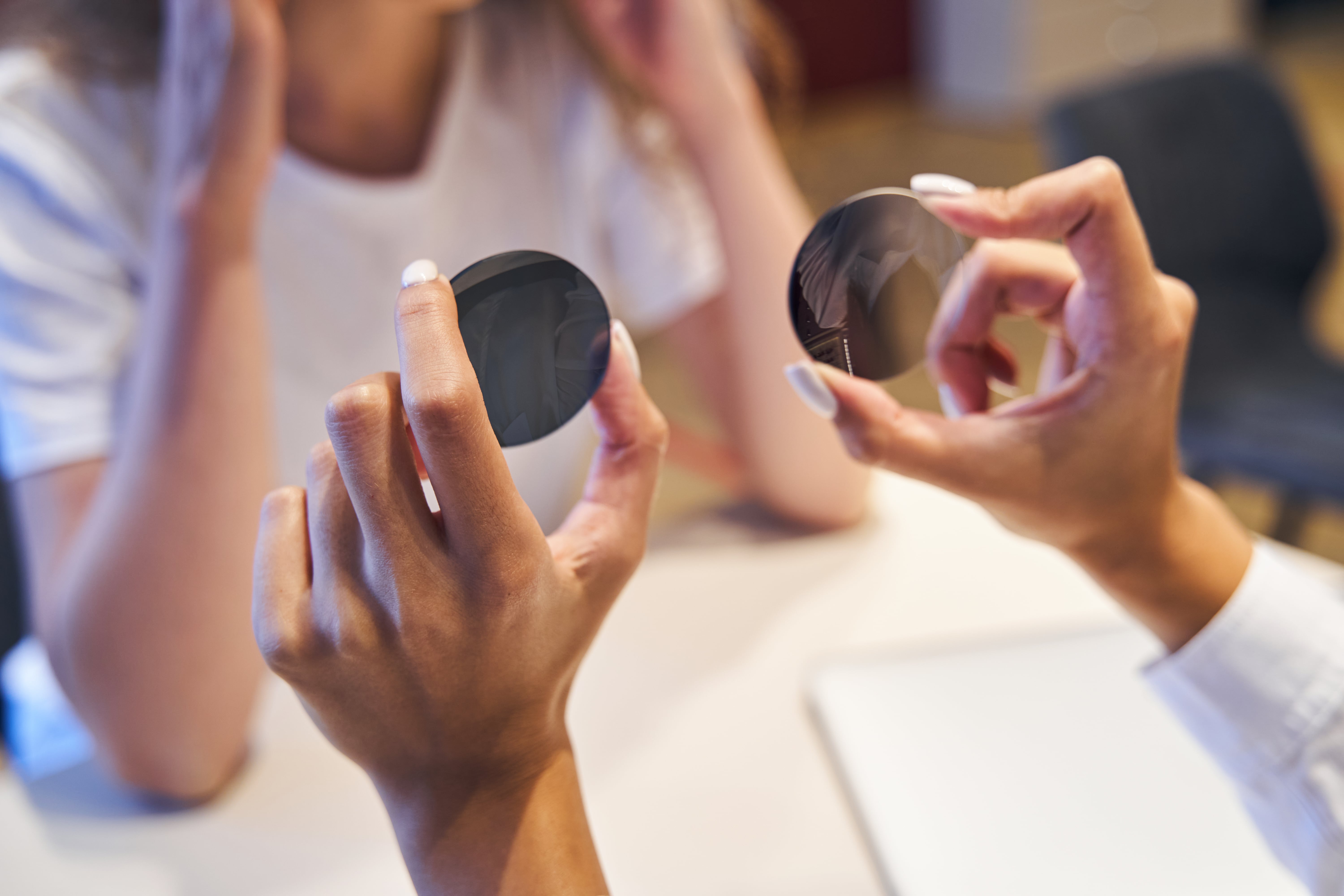 Hands holding and examining two dark circular lenses or filters