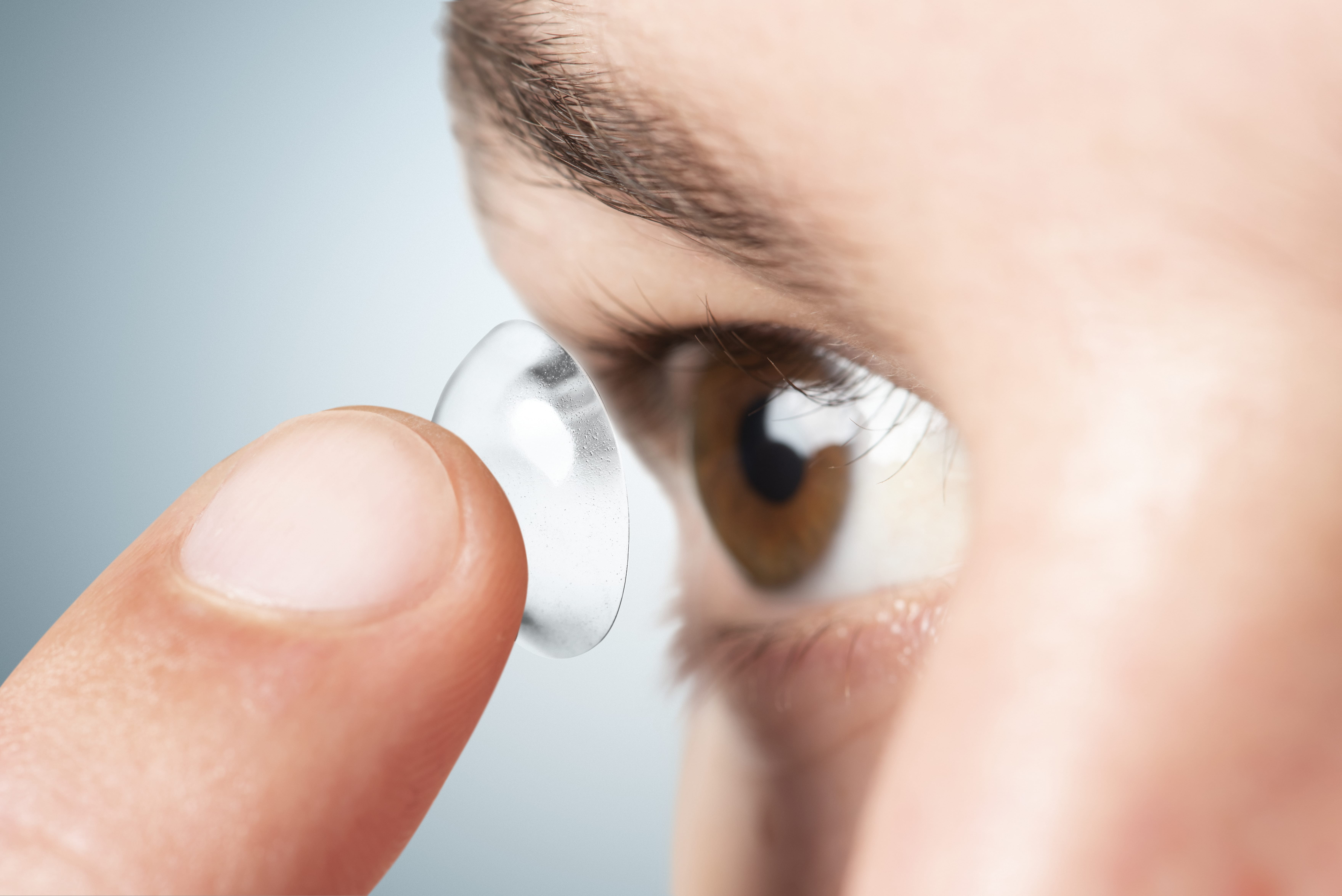 Close-up of finger inserting contact lens into brown eye